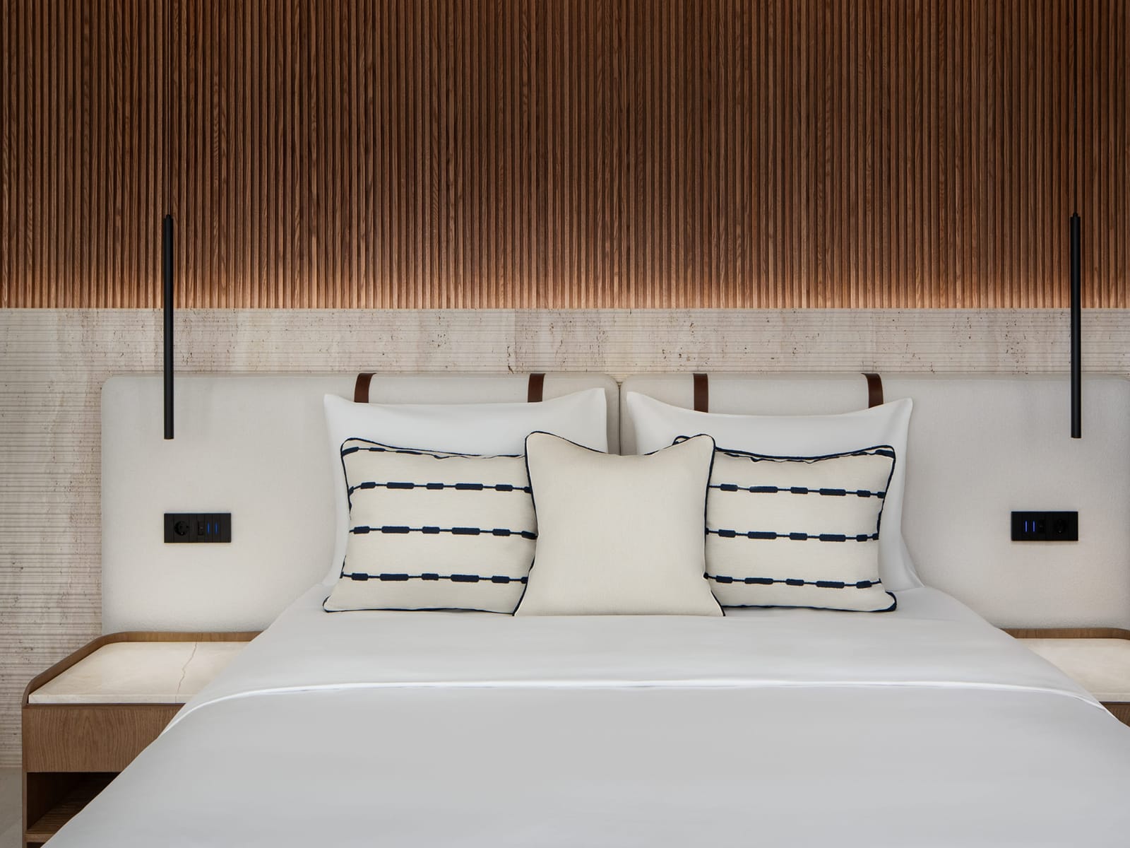Finished suite bedroom at Hotel Vione Paros, with a fluted timber headboard wall and travertine surfaces